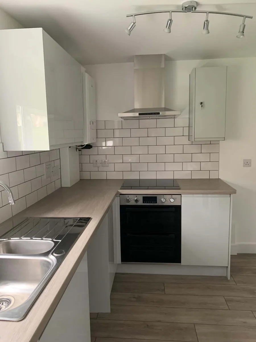 Fitted cooking area with white cabinets, tiled splashback and integrated oven.