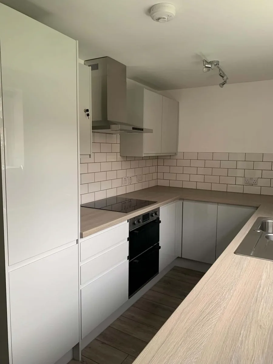 White fitted kitchen with integrated oven and light wood-effect worktops.